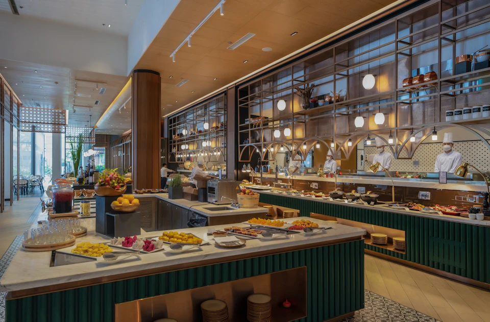 Buffet with various dishes displayed on counters in a well-lit restaurant with modern decor and open kitchen.