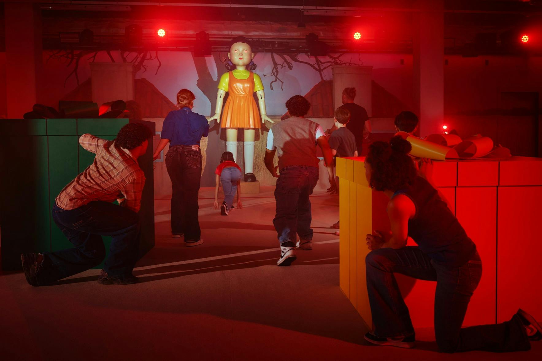 人们在类似游乐场的环境中小心翼翼地接近一个大娃娃，周围有红灯和周围的结构。