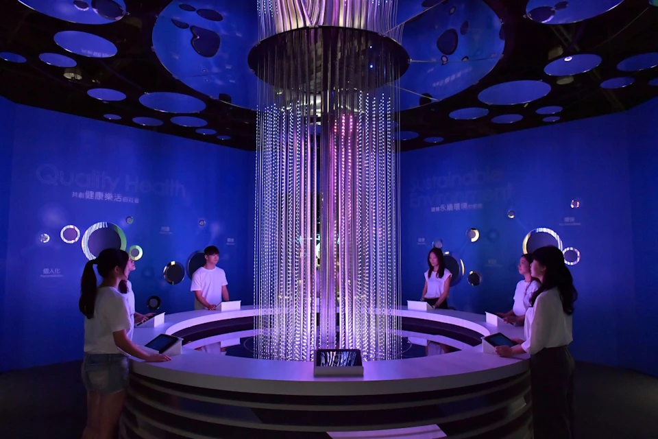 People standing around a futuristic circular installation with glowing lights in a blue-lit room.
