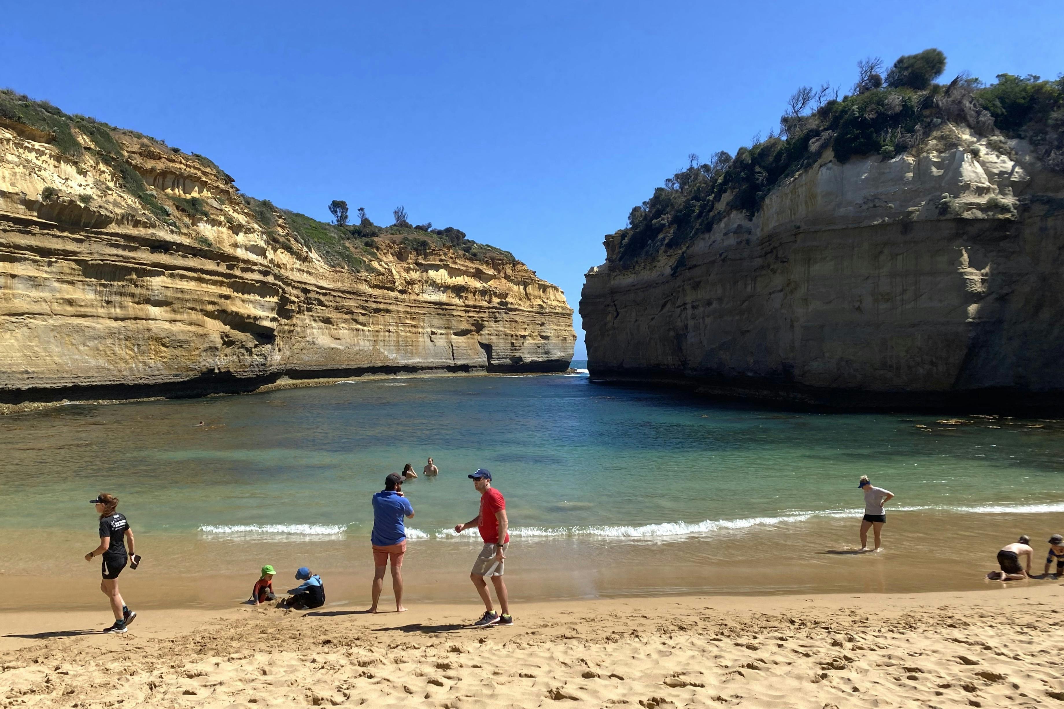 Ein Strand, eingebettet zwischen Klippen, mit Menschen, die das Wasser und den Sand unter einem klaren blauen Himmel genießen.