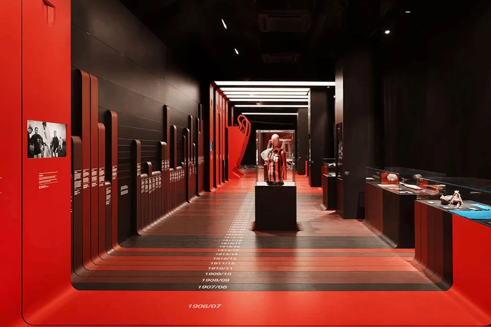 A modern exhibition space with a red and black theme, featuring displays and a mannequin in the center under bright lighting.