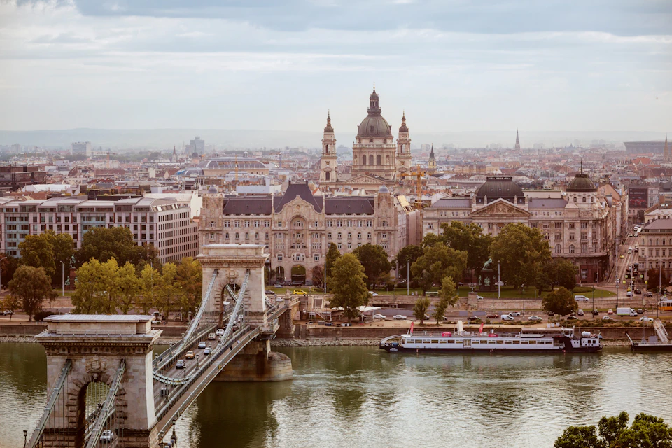 A cityscape with a historic bridge over a river in the foreground and a large domed building in the background.