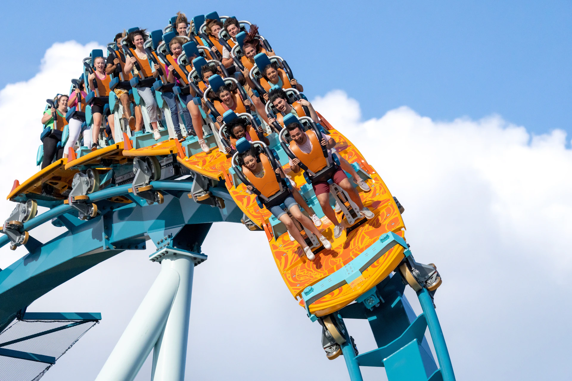 A group of people riding a large rollercoaster, descending a steep drop, all wearing safety harnesses and looking excited.