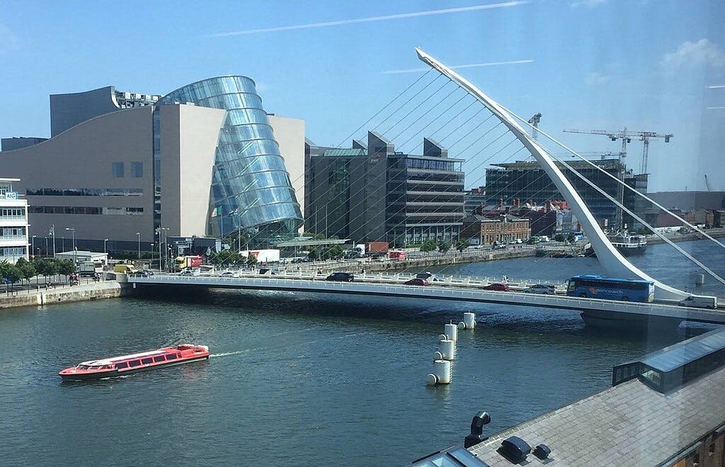 A modern bridge crosses a river with a boat below. Futuristic buildings and a construction crane are in the background.