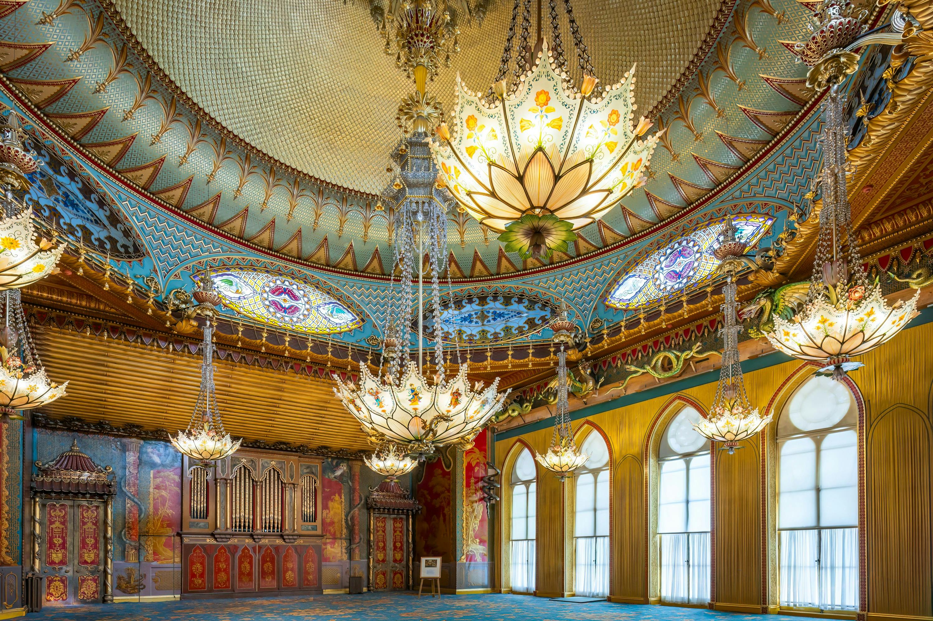 Ornate room with large, intricate chandeliers, arched windows, vibrant wall art, and a richly decorated, domed ceiling.