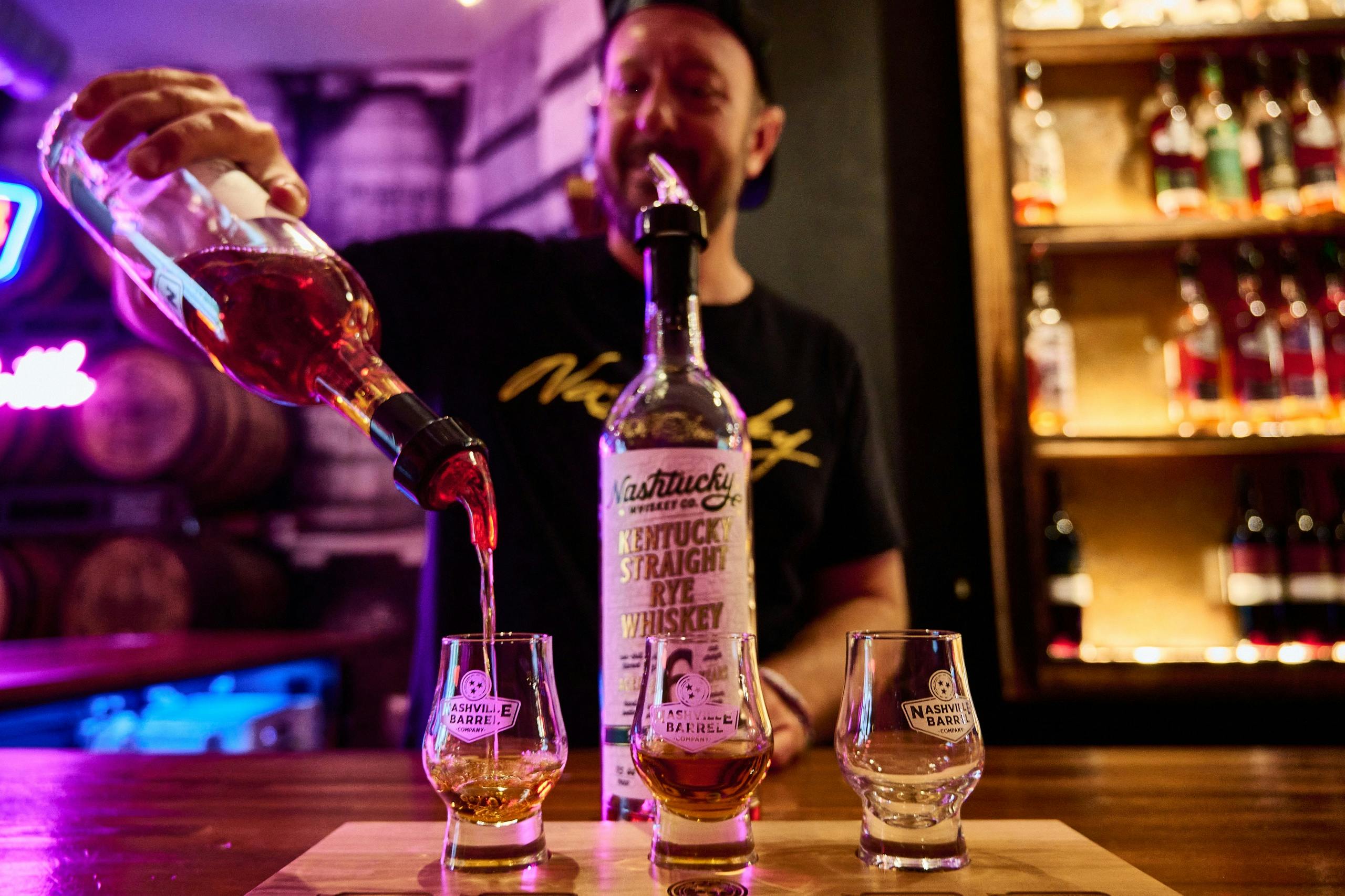 一个人将威士忌从木质表面上标有“肯塔基直黑麦威士忌”的瓶子倒入玻璃杯中。