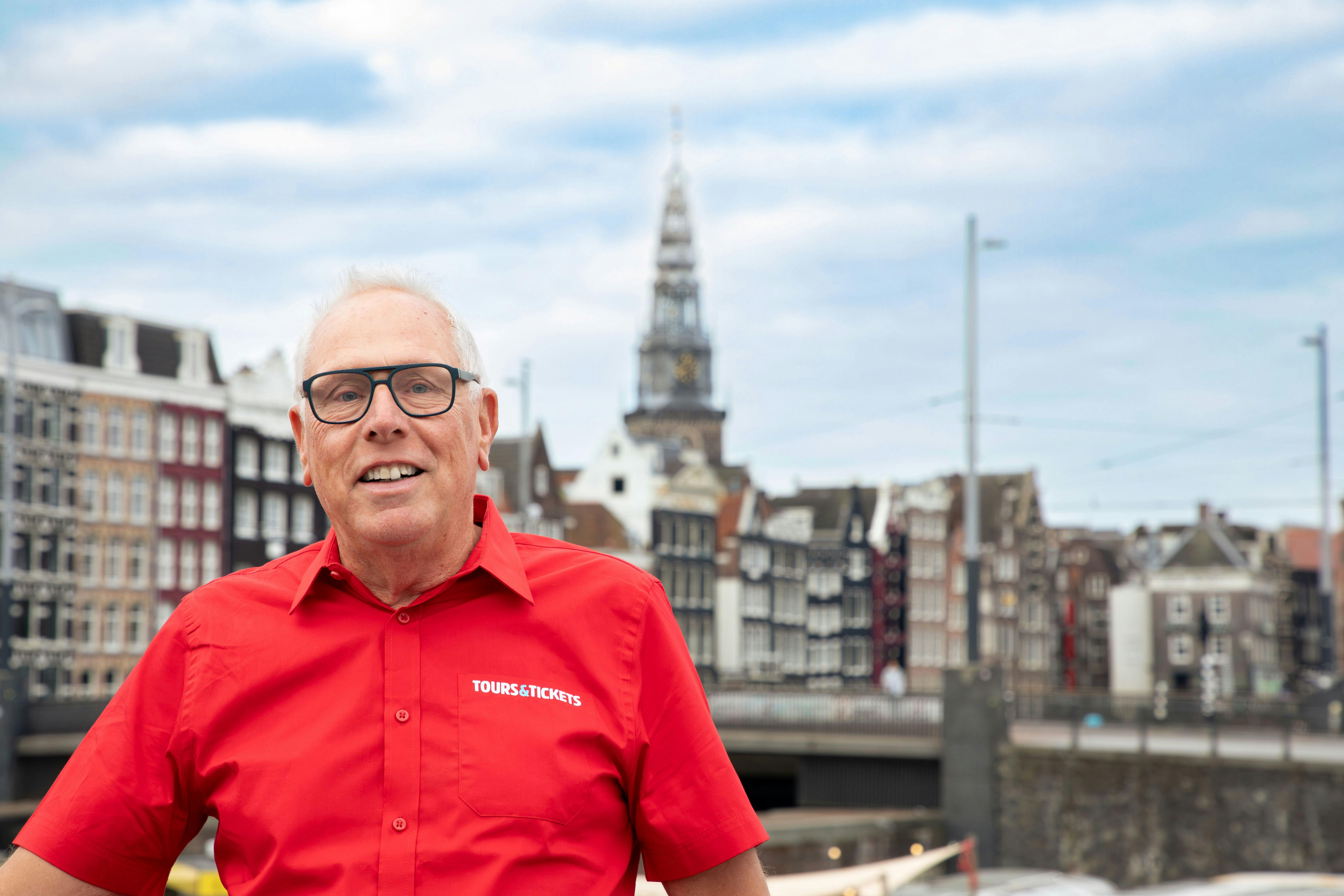 Man in red "Tours & Tickets" shirt smiling, with historic European buildings and a church tower in the background.