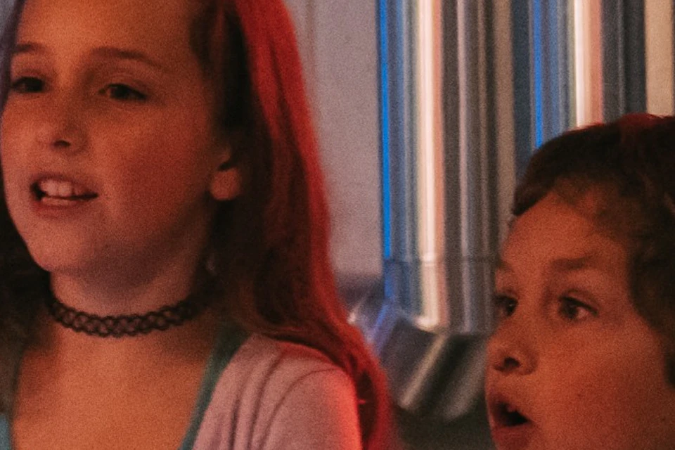 Two children interact with a light display at a science exhibit, with information panels and pipes in the background.