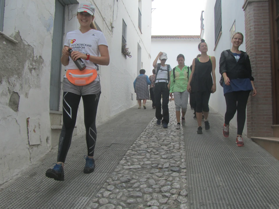 A group of people walking down a narrow, cobblestone street flanked by white buildings.