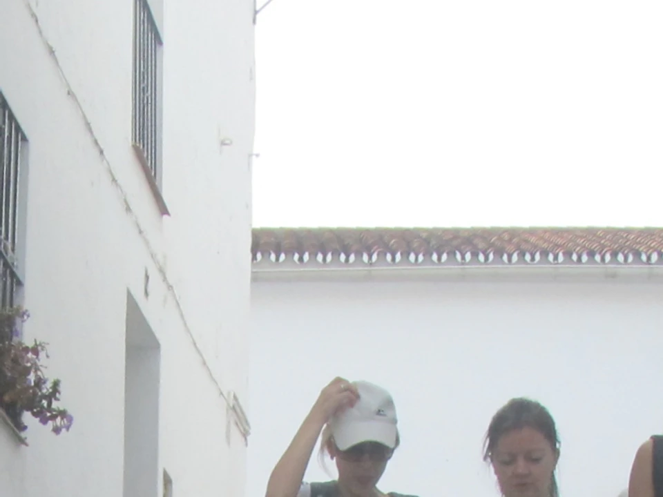 A group of people walking down a narrow, cobblestone street flanked by white buildings.