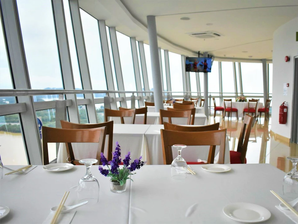 A modern restaurant with glass walls, white tablecloths, wooden chairs, and a vase of lavender flowers on a table.