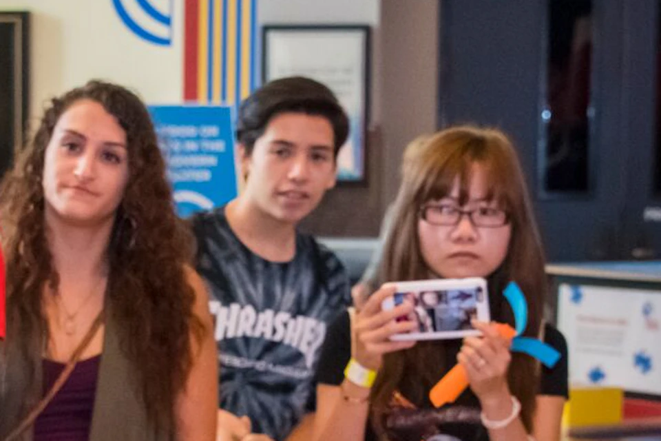 A woman holds and explains a model brain to a group of attentive people, some of whom are taking photos and videos.