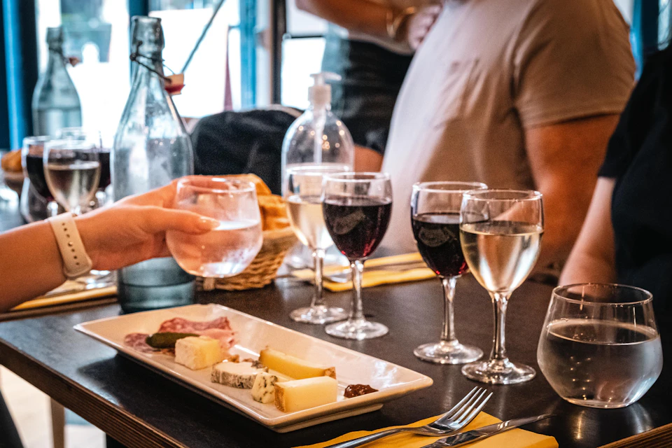 A table setting with glasses of red and white wine, a charcuterie plate, and a hand holding a glass of water.