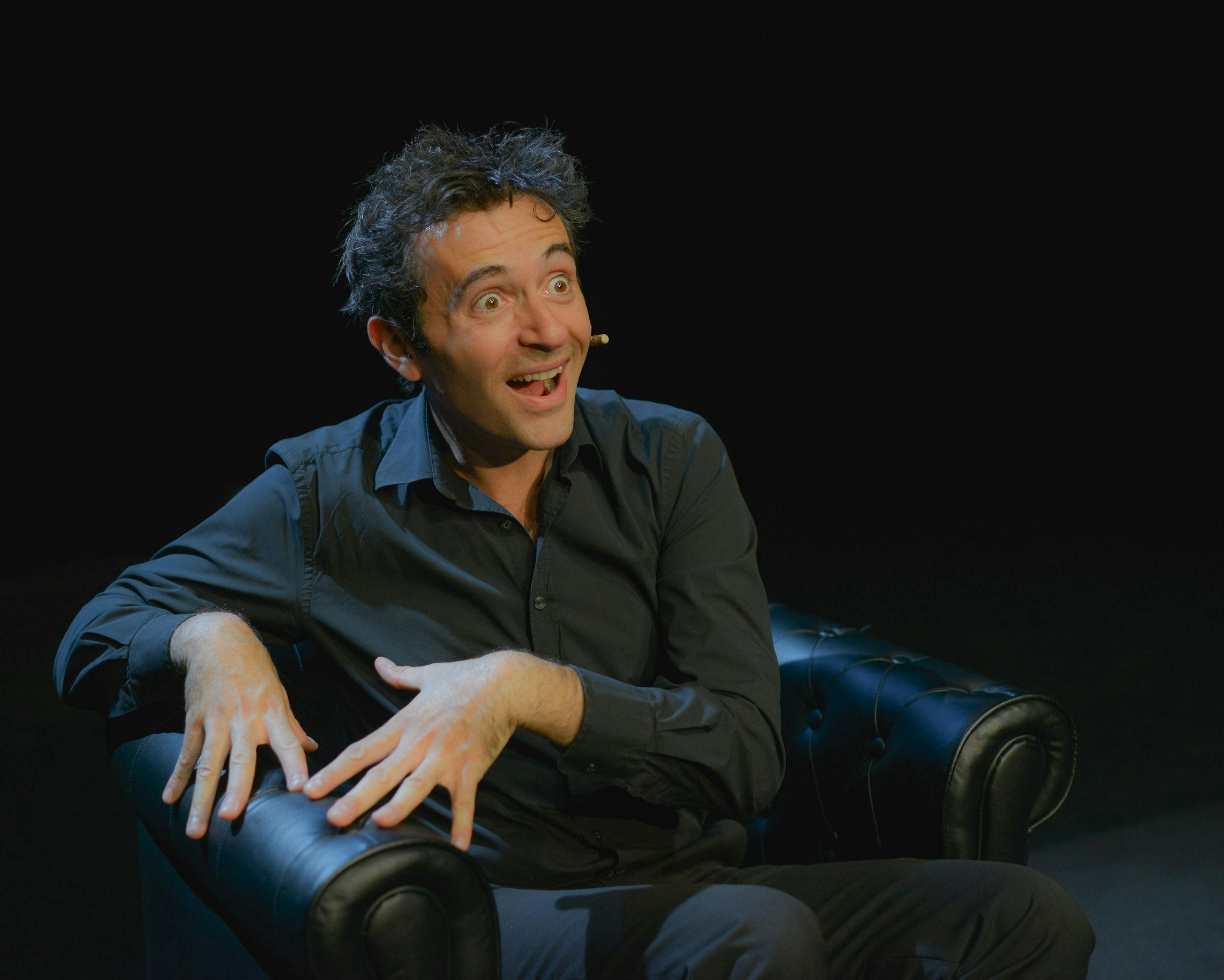 坐在黑暗的房间里，戴着耳机麦克风，做动画表情和手势的人。