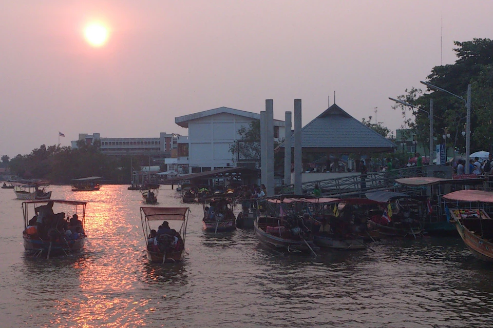 A busy waterway with boats carrying passengers under a setting sun, adjacent to buildings and a dock area.