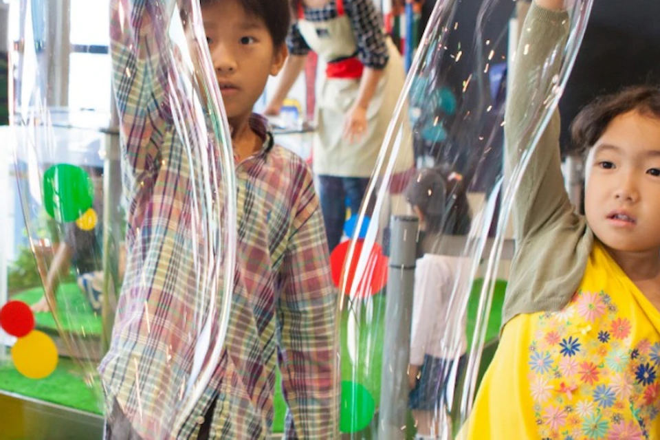 Children creating large soap bubbles using wands at an interactive exhibit.
