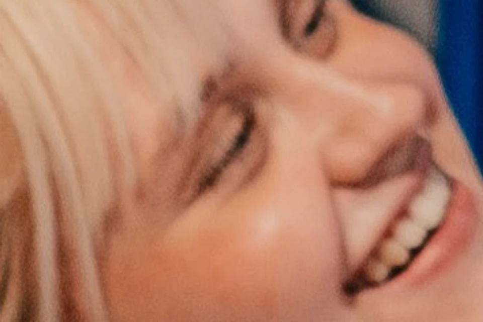 A person wearing a white shirt smiles and leans against a blue wall with concentric circle patterns. Geometric shapes are visible in the background.