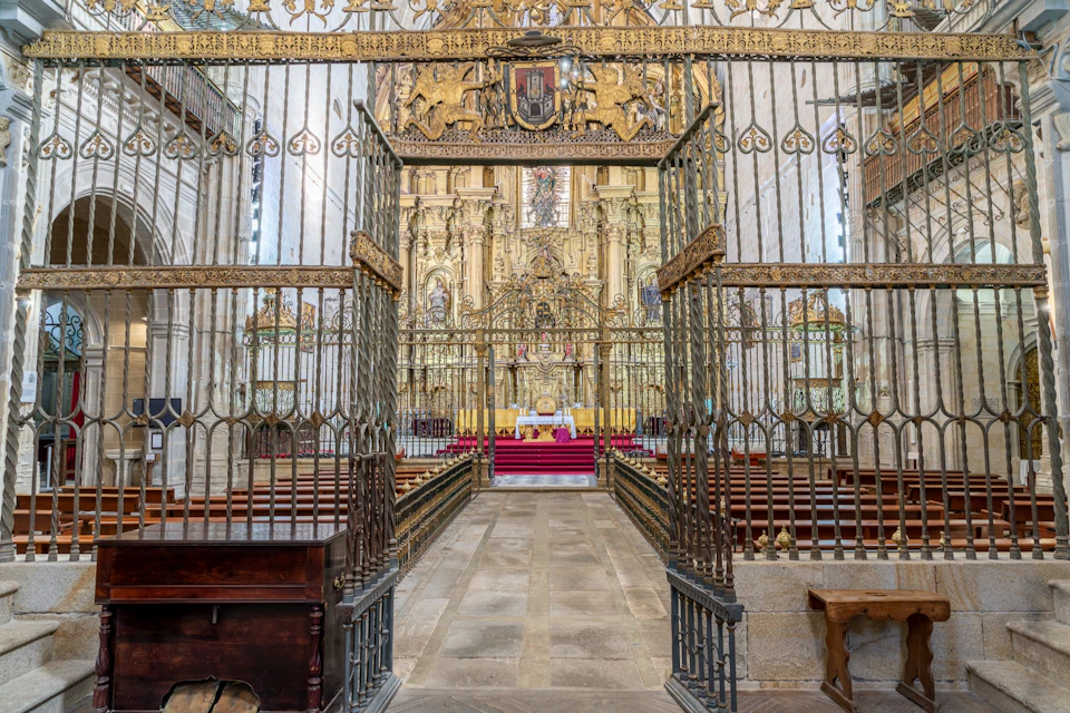 Elaborate church interior with ornate golden altar, iron gate, and rows of benches, showcasing detailed architecture.