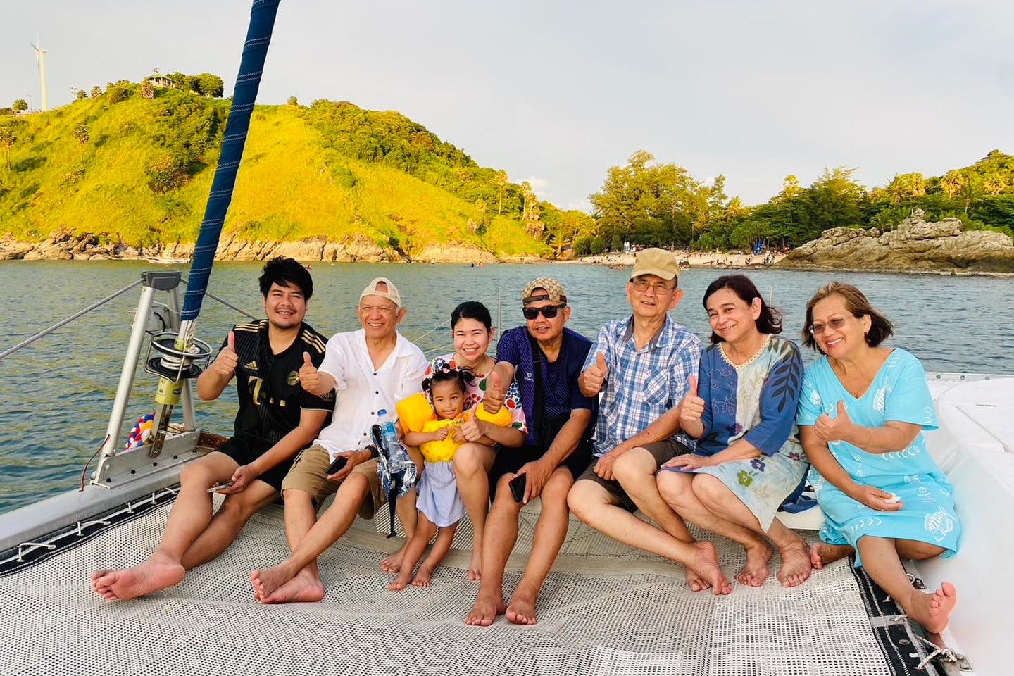 Έξι άτομα, συμπεριλαμβανομένου ενός παιδιού, κάθονται σε μια βάρκα με μια γραφική θέα στους καταπράσινους λόφους στο παρασκήνιο, και όλοι χαμογελούν.