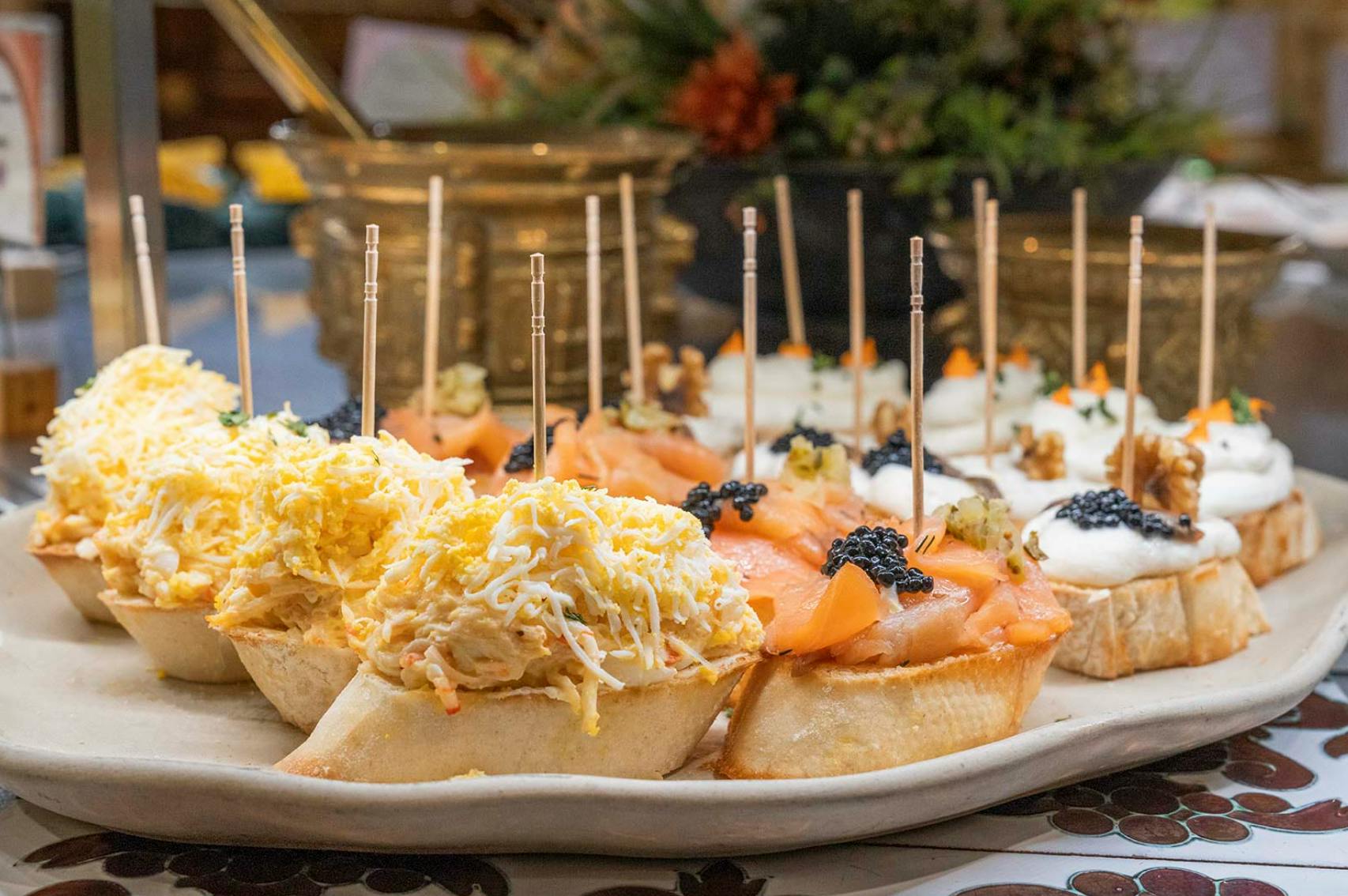 Un piatto di tapas assortite con condimenti come formaggio tritato, salmone e caviale, guarnito con spiedini.