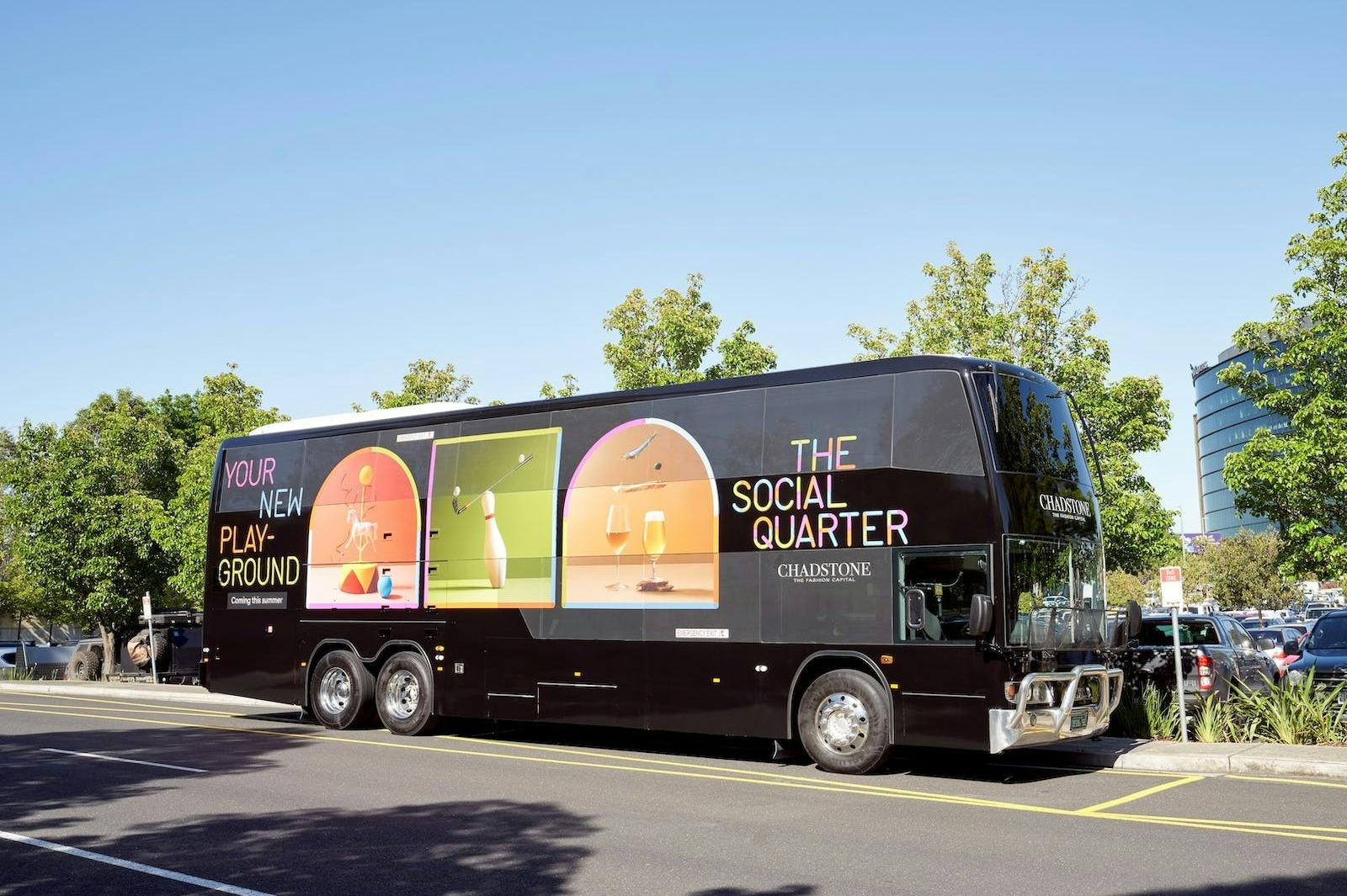 Un autobus nero a due piani con pubblicità colorate e testi che promuovono "The Social Quarter" di Chadstone è parcheggiato in una strada.