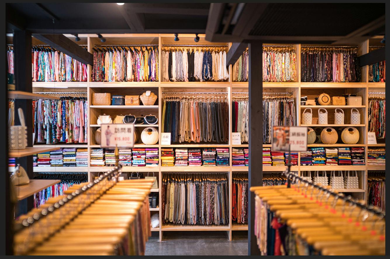 A clothing and fabric store with shelves of neatly arranged fabrics and garments, and racks of clothes in the foreground.