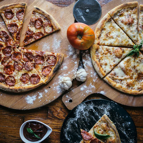 Två pizzor, en pepperoni och en ost, på träbrädor med tomat, vitlök och en liten sås.