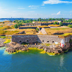 Historic fortress with stone walls surrounded by water and greenery under a blue sky with scattered clouds.
