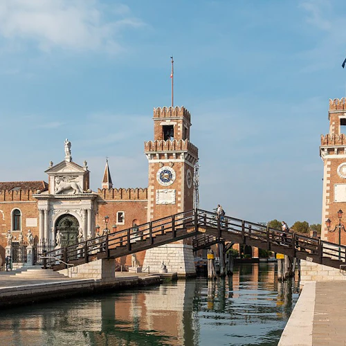 Två tegeltorn med urtavlor, förbundna med en träbro över en kanal, med människor som går i närheten.
