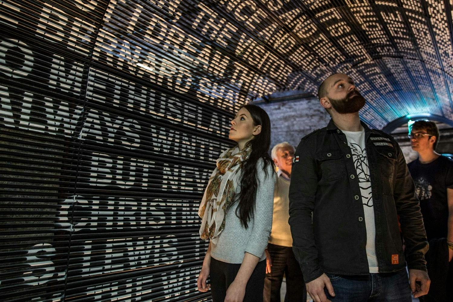 A group of people looking up in an illuminated tunnel with text projected on the walls and ceiling.