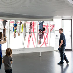 Människor står och observerar en stor funhouse-spegel som visar förvrängda reflektioner.