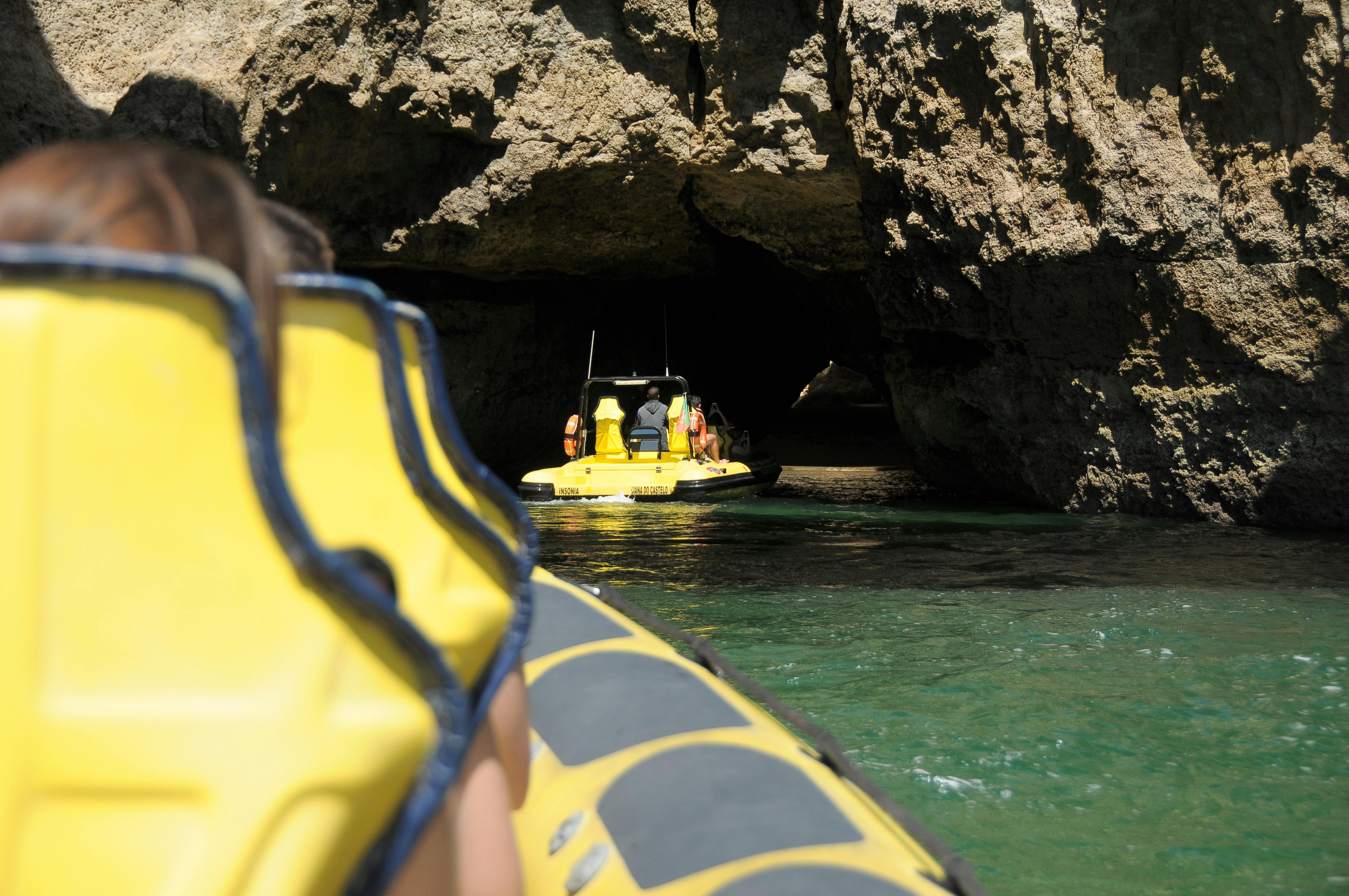 Lidé ve žlutých nafukovacích člunech se blíží ke skalnatému vchodu do jeskyně nad zelenou vodou.
