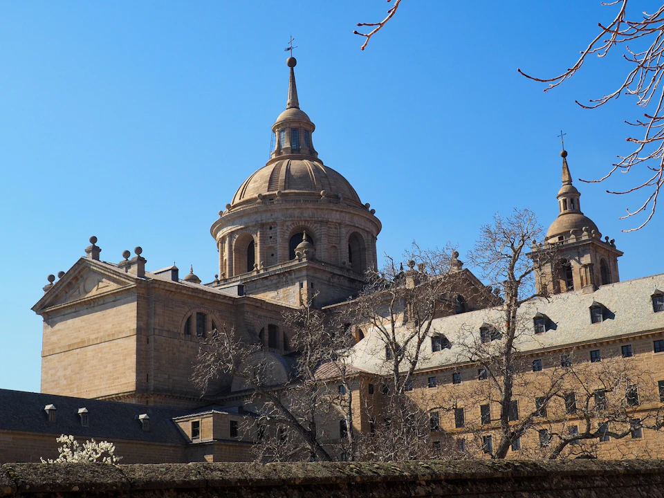 Stone building with domed towers under a clear blue sky, surrounded by bare trees.