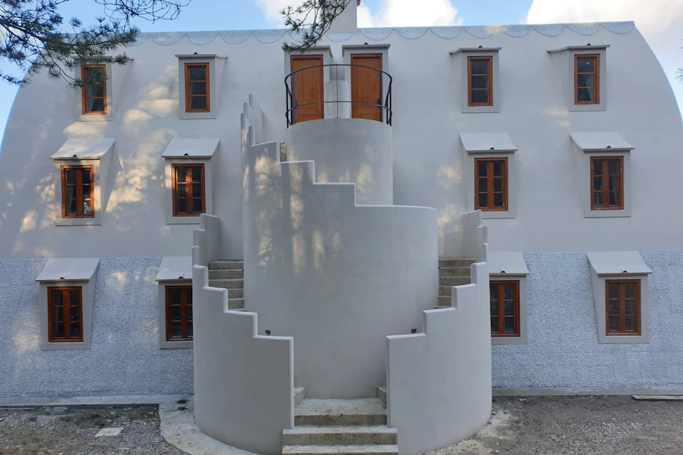 A white building with wooden windows and a central spiraling staircase leading to a small balcony with doors.