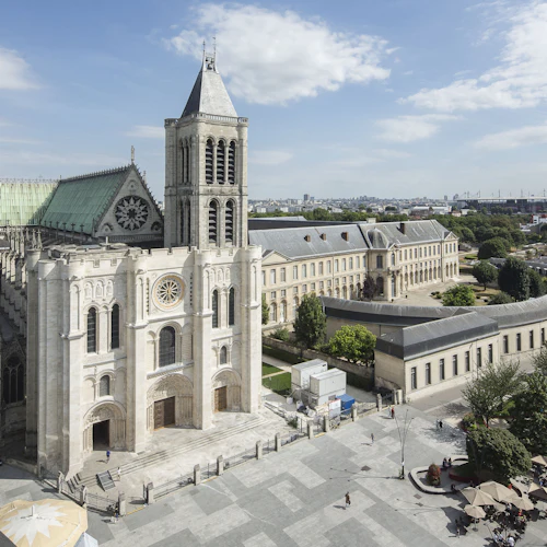 En stor, historisk katedral med grönt tak och högt torn, omgiven av träd och intilliggande byggnader en ljus dag.