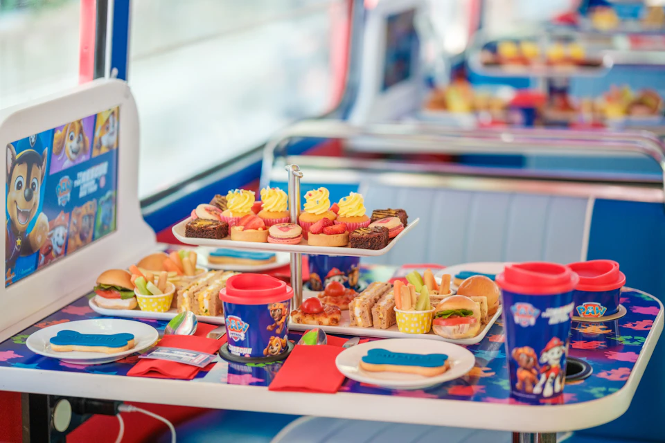 A colorful table set with sandwiches, cupcakes, and themed cups in a retro diner setting.