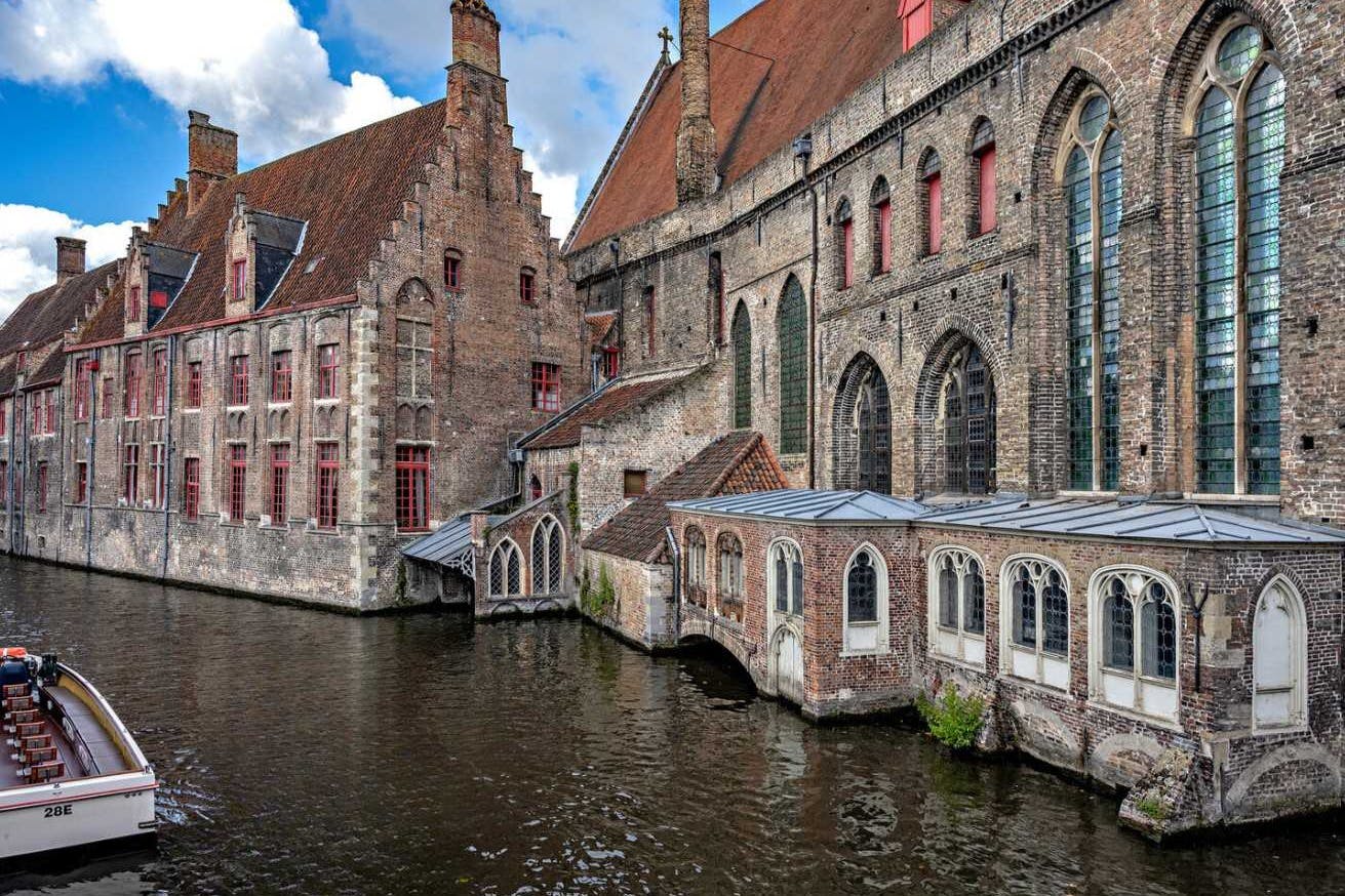 历史悠久的砖建筑，沿着蓝天下的运河有红色的窗户。