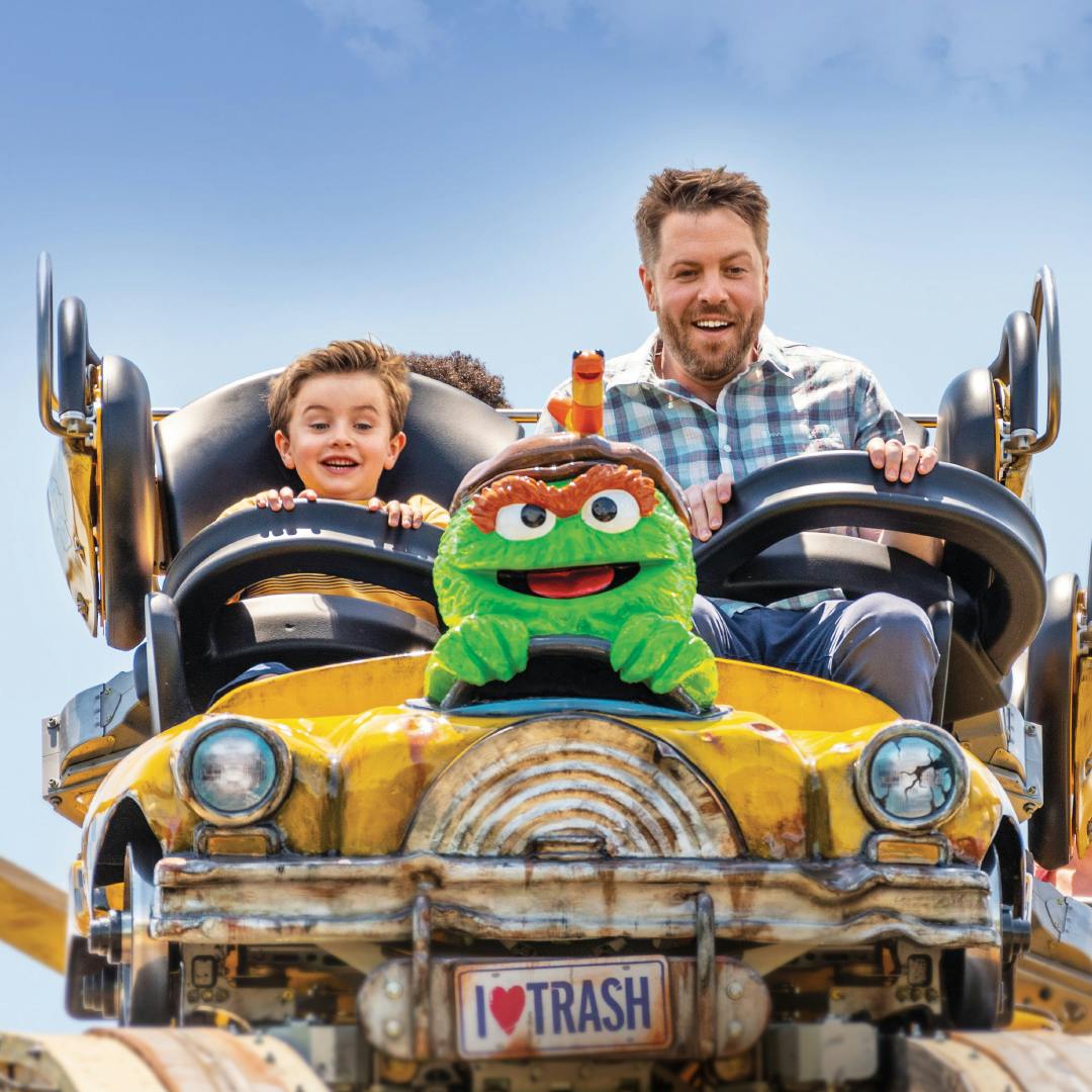 一名男子和男孩兴奋地乘坐黄色过山车，主题是绿色人物和“I ♥ Trash”车牌。