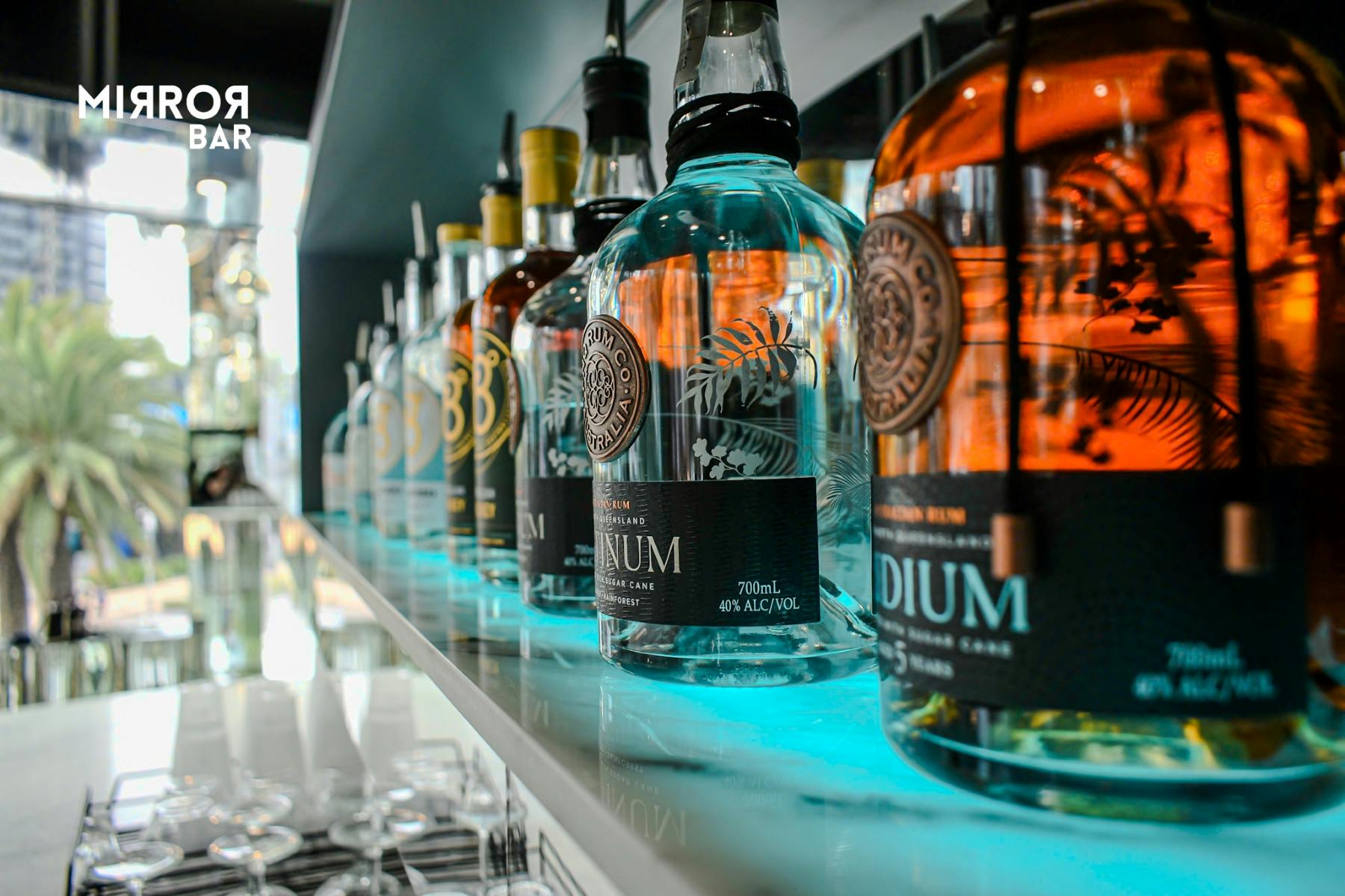 バーの明るい棚に展示されている複数のプレミアムリキュアボトルのクローズアップ。複雑なラベルとデザインが特徴です。