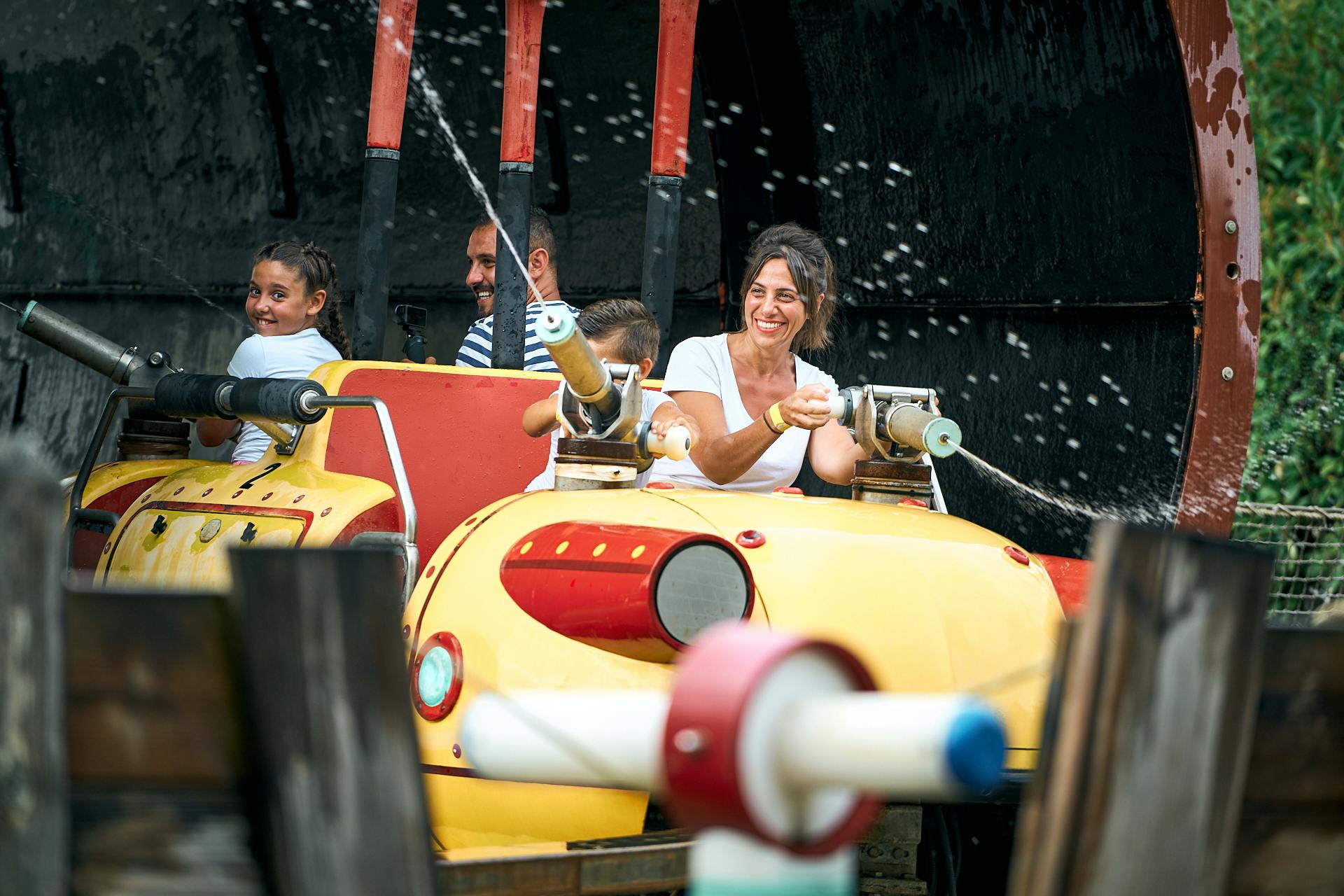 Lidé se baví při jízdě na vodě a stříkají z vodních děl proudy vody. Všichni se usmívají a věnují se aktivitě.