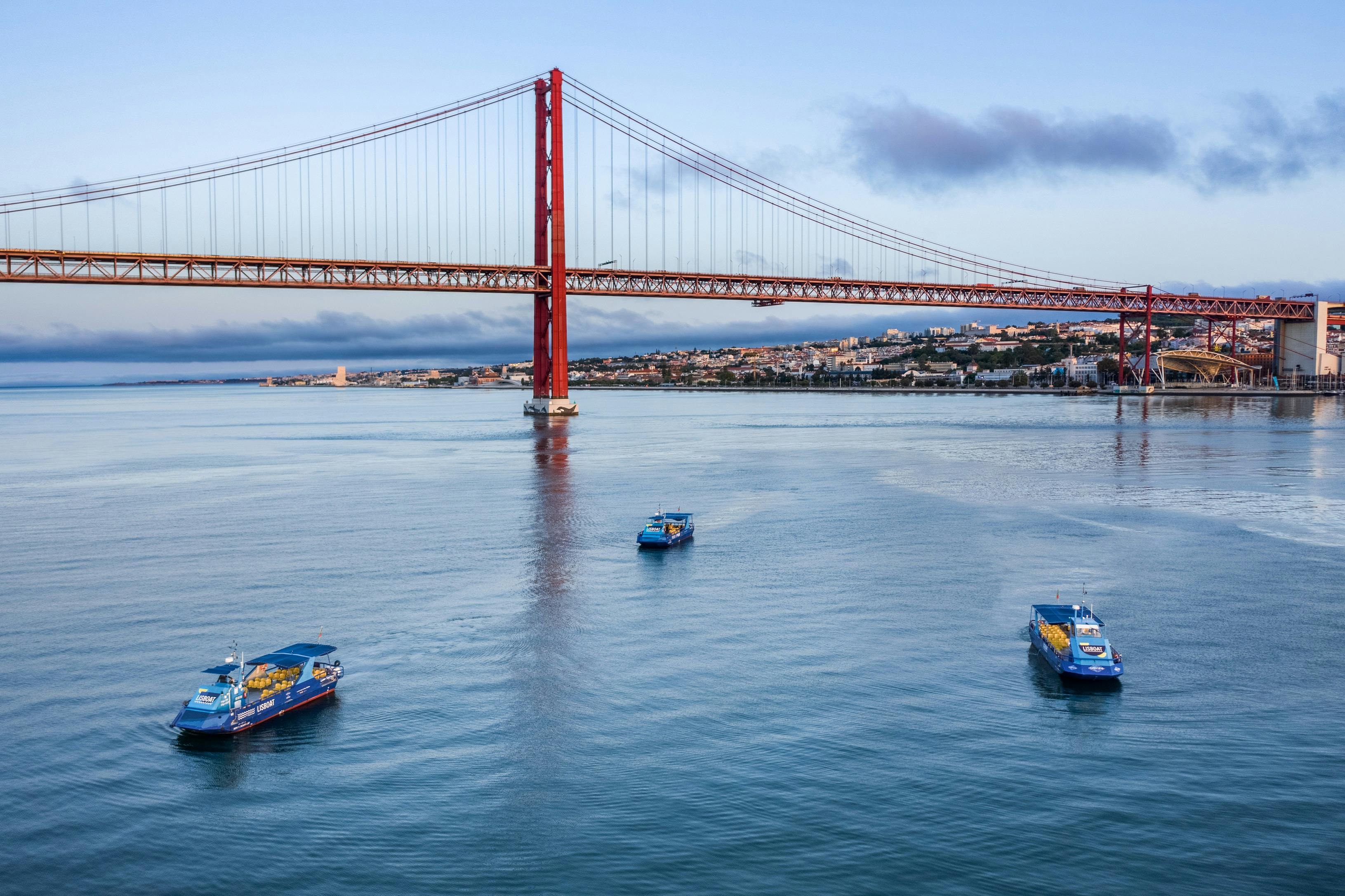 붉은 현수교를 배경으로 한 잔잔한 강에서 세 척의 투어 보트를 타고 강둑에서 도시 풍경을 감상해보세요.