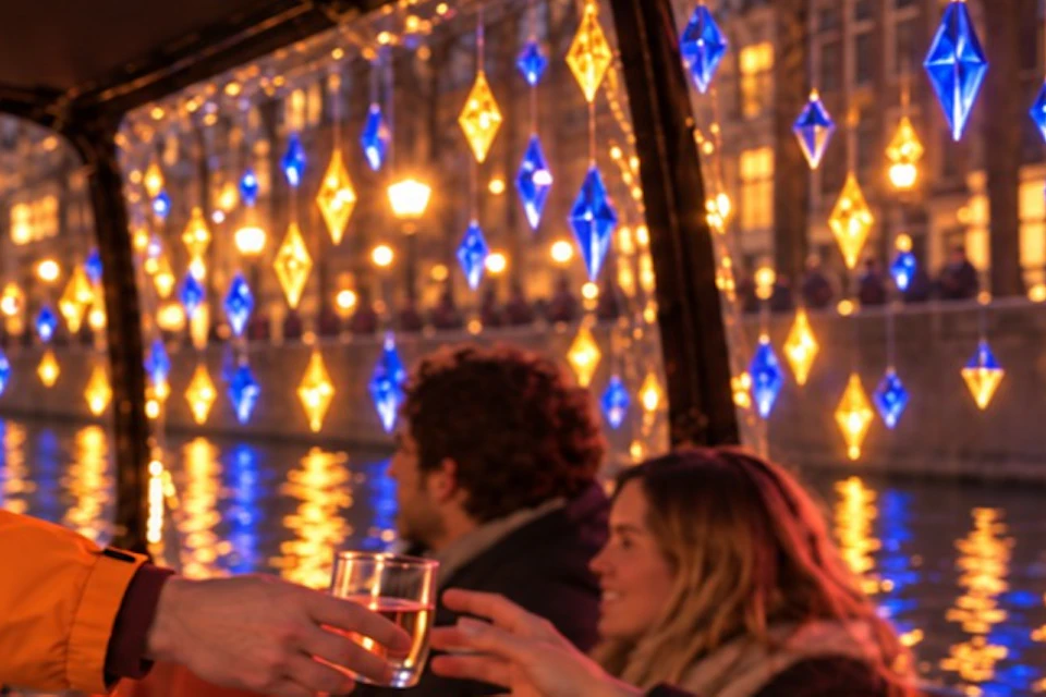 People enjoying a drink on a cozy boat with decorative lights and bottles of wine displayed in an ice bucket.