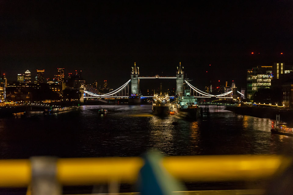 Tower Bridge illuminated at night with reflections on the Thames and buildings in the background.