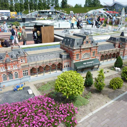 En miniatyrmodell av Groningens centralstation omgiven av små träd och blommor, observerad av människor i en park.