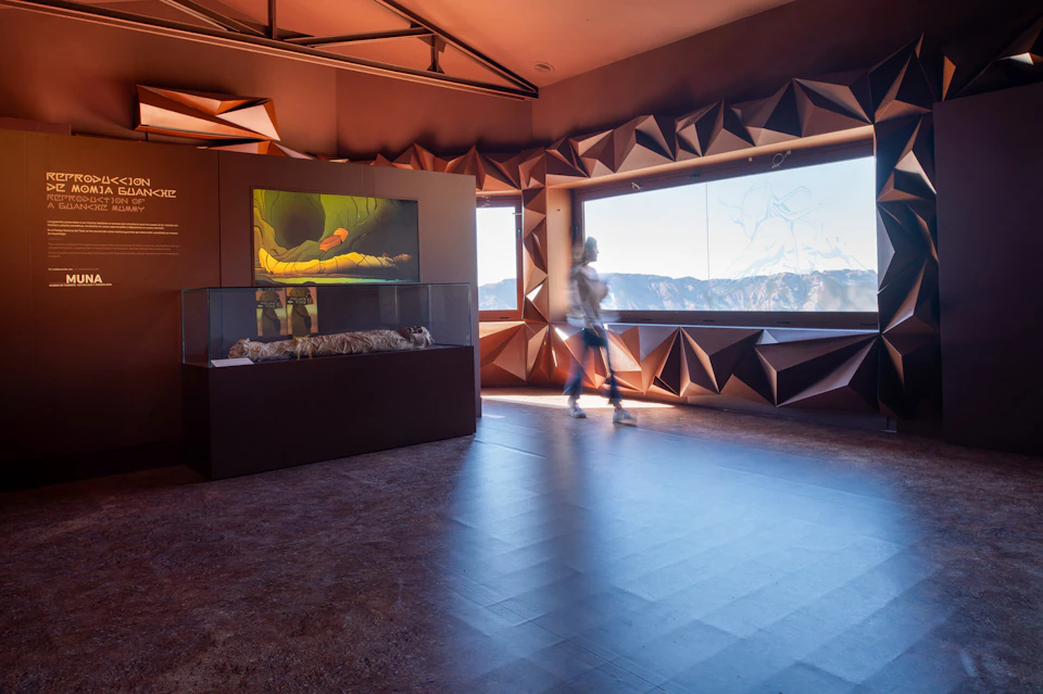 A person walking past an indoor exhibit featuring nature displays, with large windows showing a mountainous landscape.