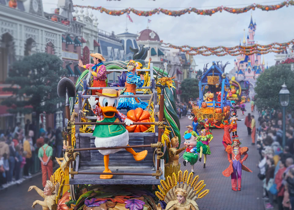 A parade featuring colorful floats, with Donald Duck on one of them, in a festive street decorated with banners and garlands.