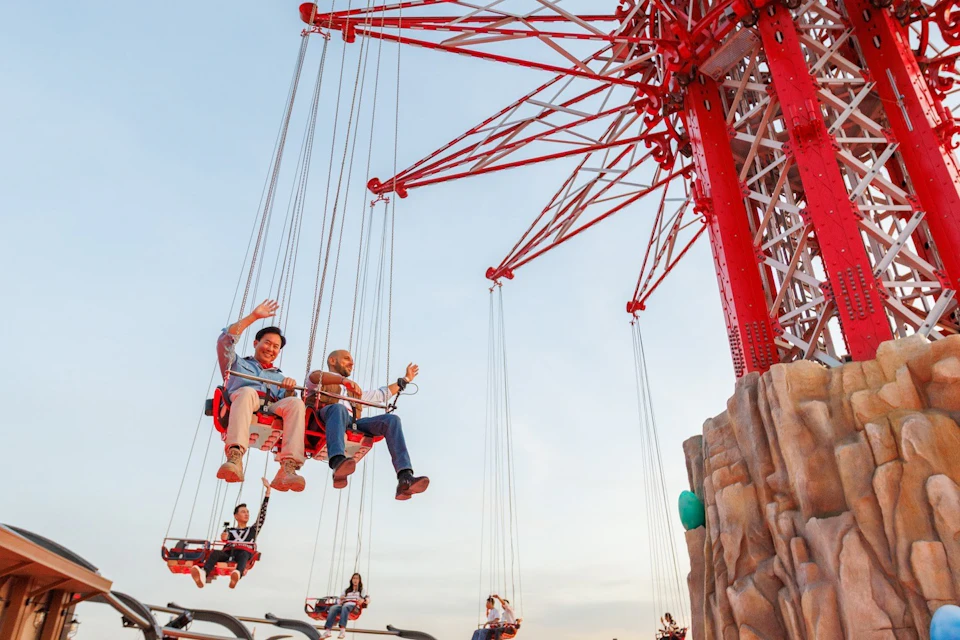 People enjoying a swing ride at a fairground, suspended in mid-air against a clear sky.