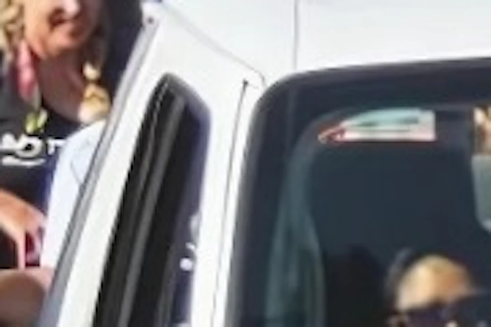 A white open tour van with passengers drives along a palm-lined street on a sunny day.