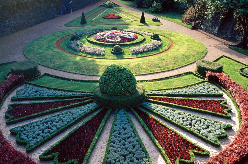 対称的な花壇、生け垣、小道があり、円形と三角形のデザインを特徴とする、細心の注意を払って造園された庭園。