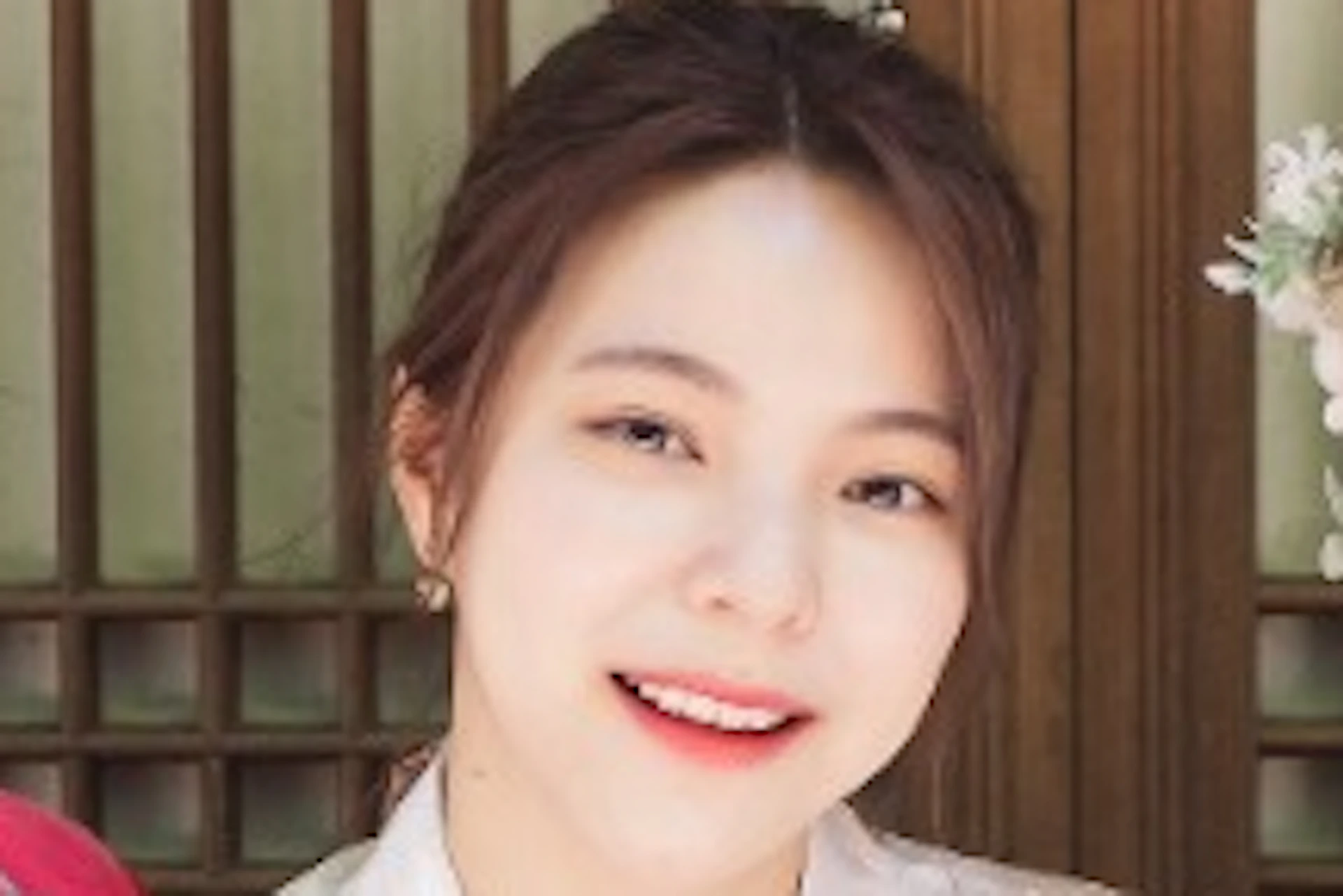 Three women in traditional Korean hanbok attire sitting together in front of a wooden door, smiling.